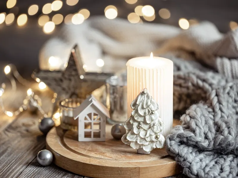 White winter scene candles next to a grey blanket and blurry lights on the background.