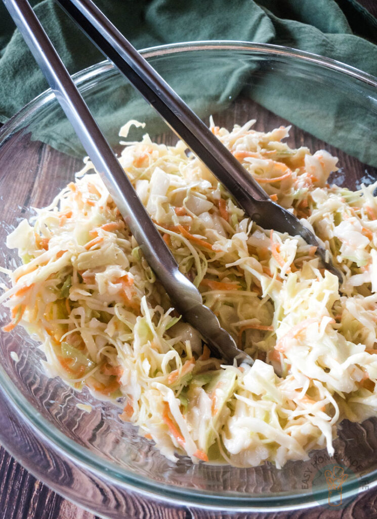 Copycat popeyes coleslaw dressing in a glass bowl with metal serving tongs.