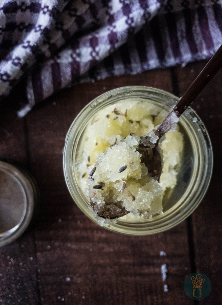 Lavender salt scrub in a jar with a copper spoon dipped in it.