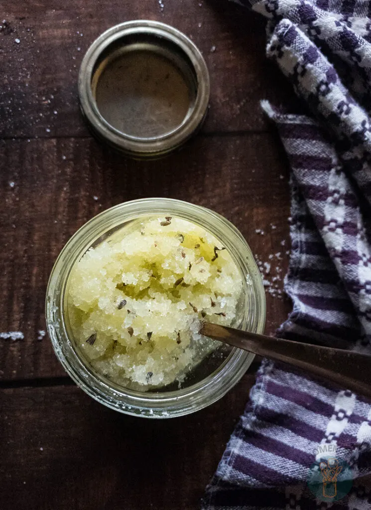 Lavender salt scrub in a jar with a spoon next to an empty jar.