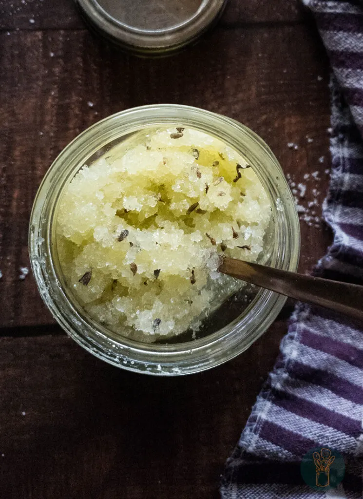 Lavender salt scrub in a jar with a spoon on a wooden table.