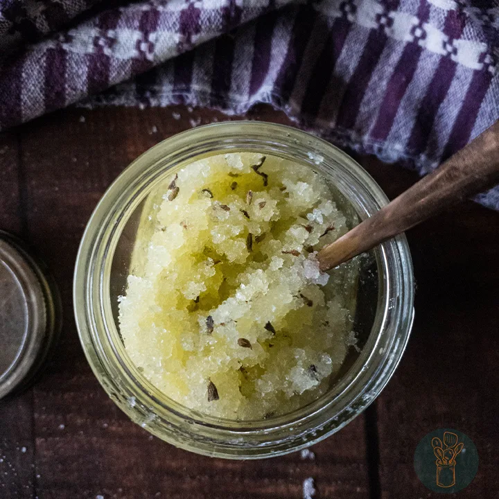 Lavender salt scrub in a jar with a spoon dipped in it on top of the table.