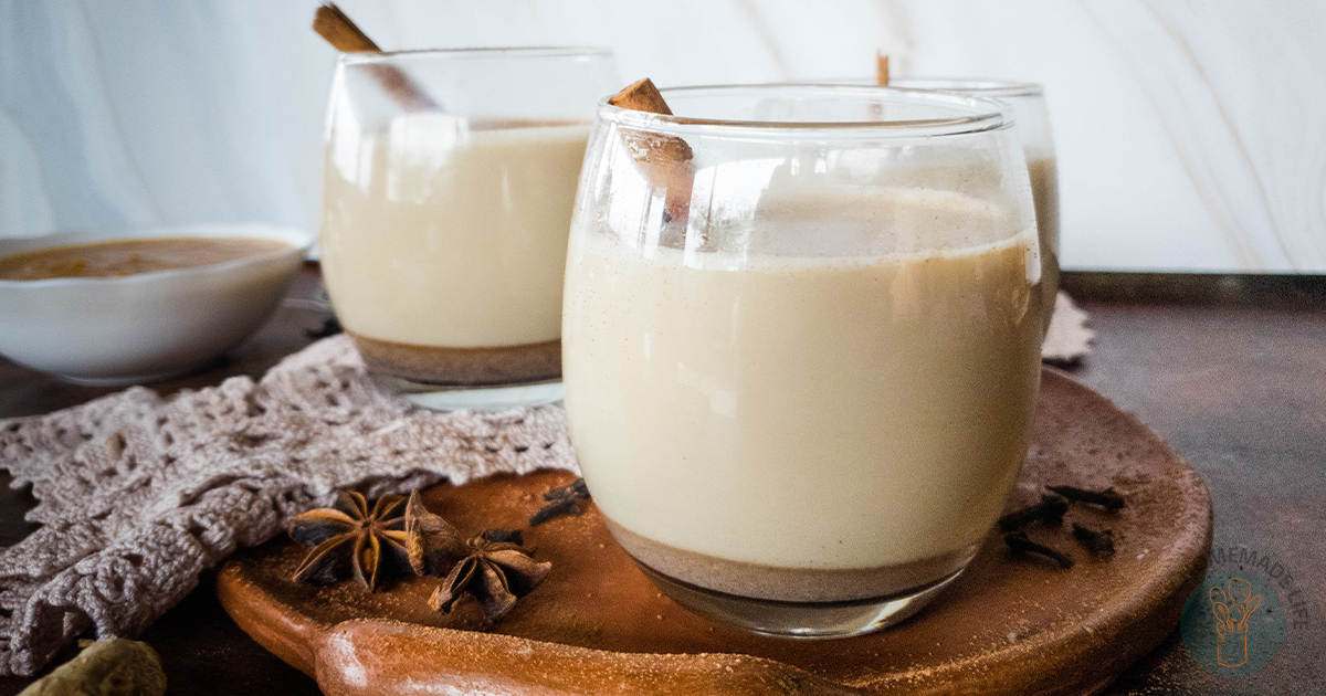 Three glasses of pumpkin chai latte with cinnamon sticks on a clay plate next to a white bowl with brown syrup.