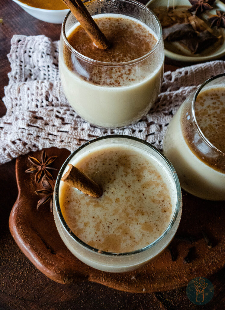 Three glasses of pumpkin chai latte with cinnamon sticks on a clay plate with crochet napkin.