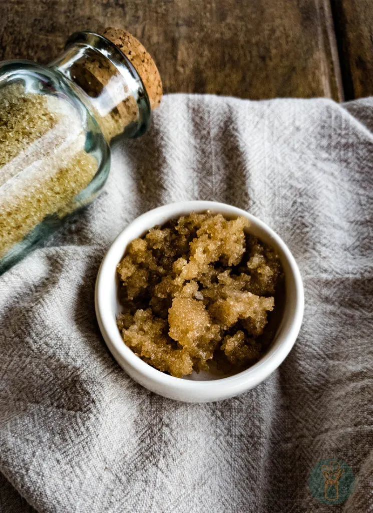 A bowl of brown sugar lip scrub next to a glass jar.