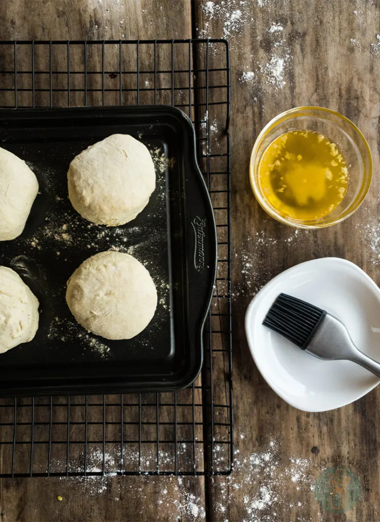 Biscuit dough on a baking sheet next to a bowl of olive oil.