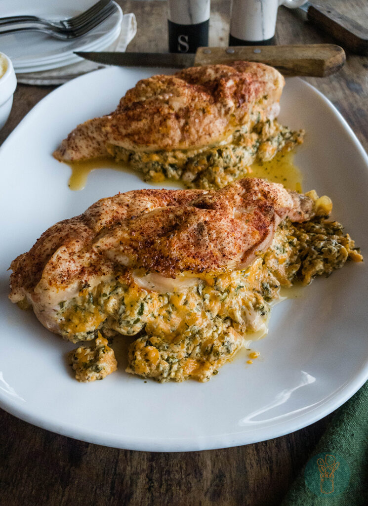 Two chicken breasts on a white plate stuffed with spinach and cheese.