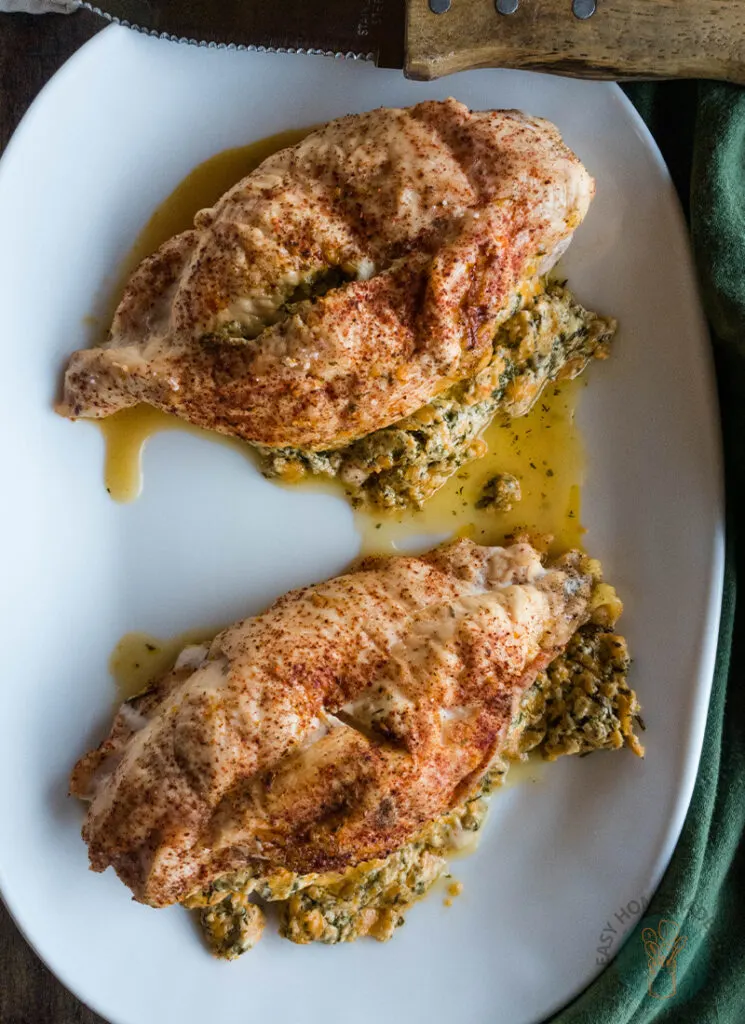 Two stuffed chicken breasts on a plate next to a knife.