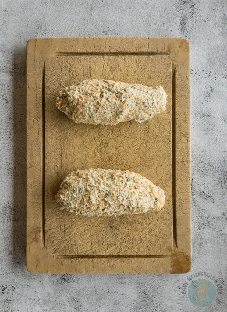 Two breaded chicken breasts on a wooden cutting board.