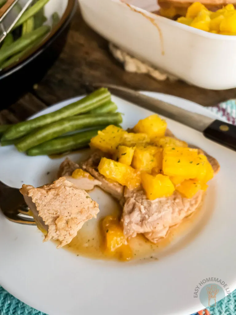 Pineapple teriyaki pork chops oven baked on a plate with a fork holding a bite above
