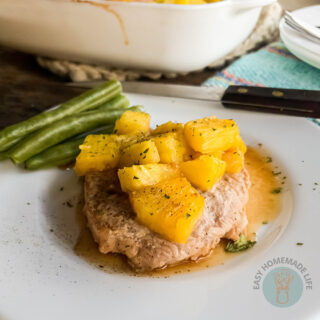 baked hawaiian pork chop on plate with green beans, knife, blue cloth and casserole dish in background