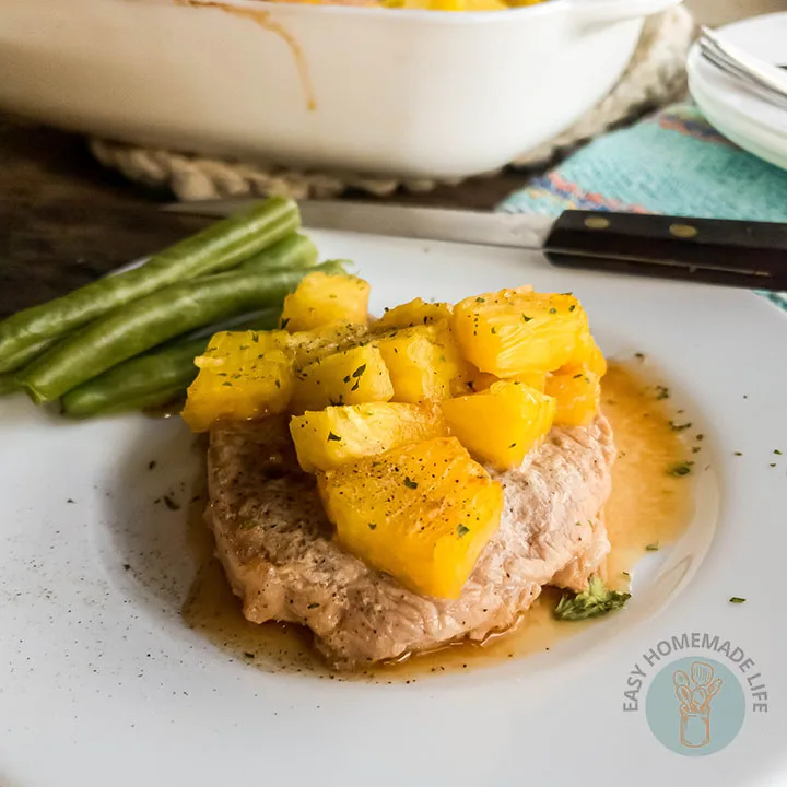 Pineapple teriyaki pork chop with cilantro and green beans garnish and a knife on the side in a white plate with turquoise towel.