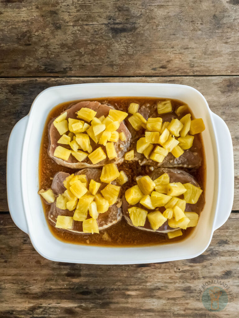 Pineapple teriyaki pork chops being marinated in a white baking dish.