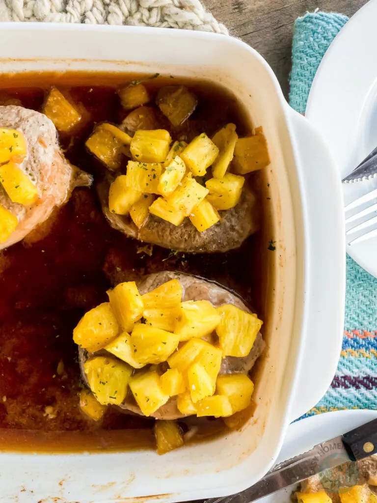 Pineapple teriyaki pork chops in a white baking dish next to a plate.