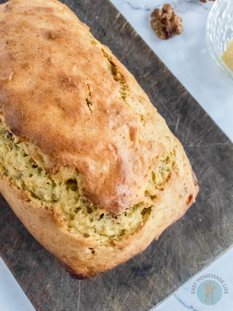 A whole loaf of banana bread on a wooden chopping board next to a walnut.