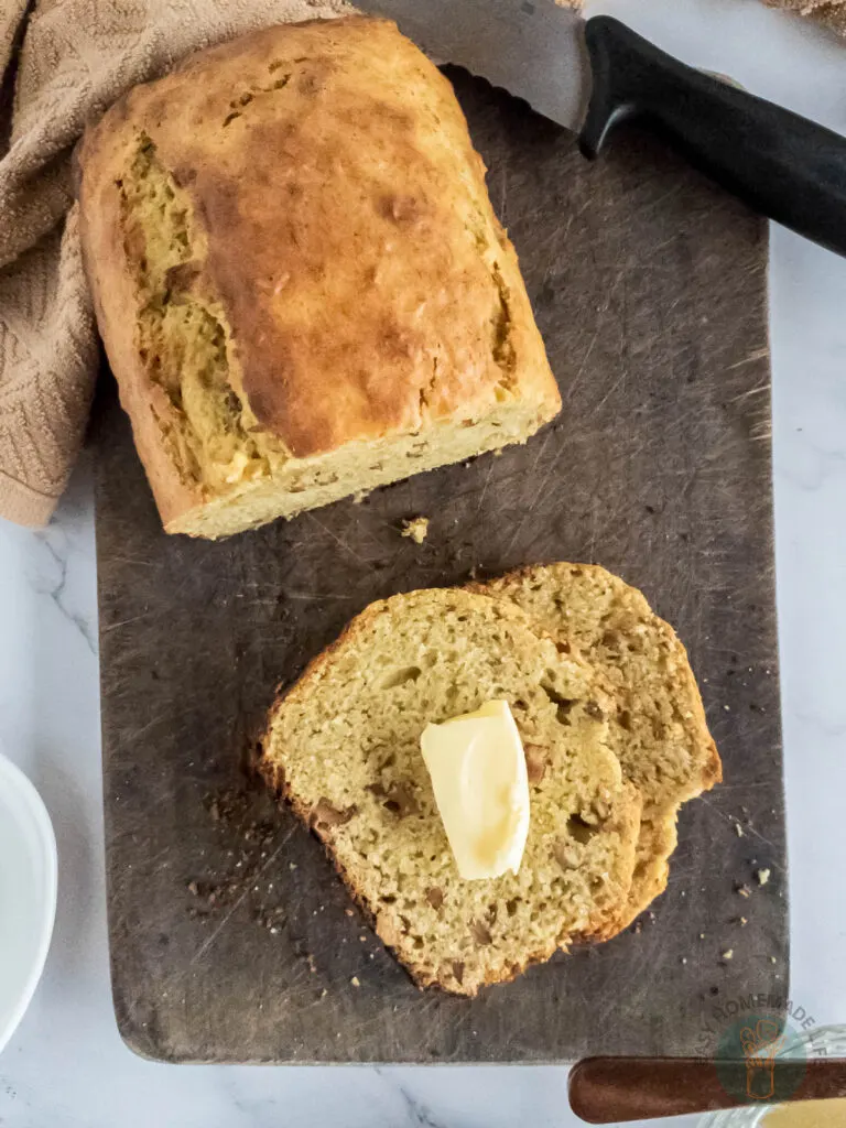A half loaf of banana bread. One thin slice of banana bread next to it with a slice of butter.