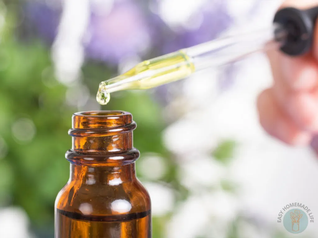 close up of glass dropper above an amber bottle of essential oil pain blend