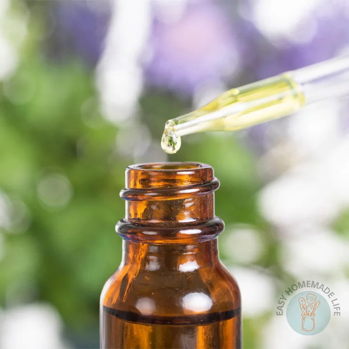 A glass dropper directed to the mouth of the bottle with the essential oil coming out of it.