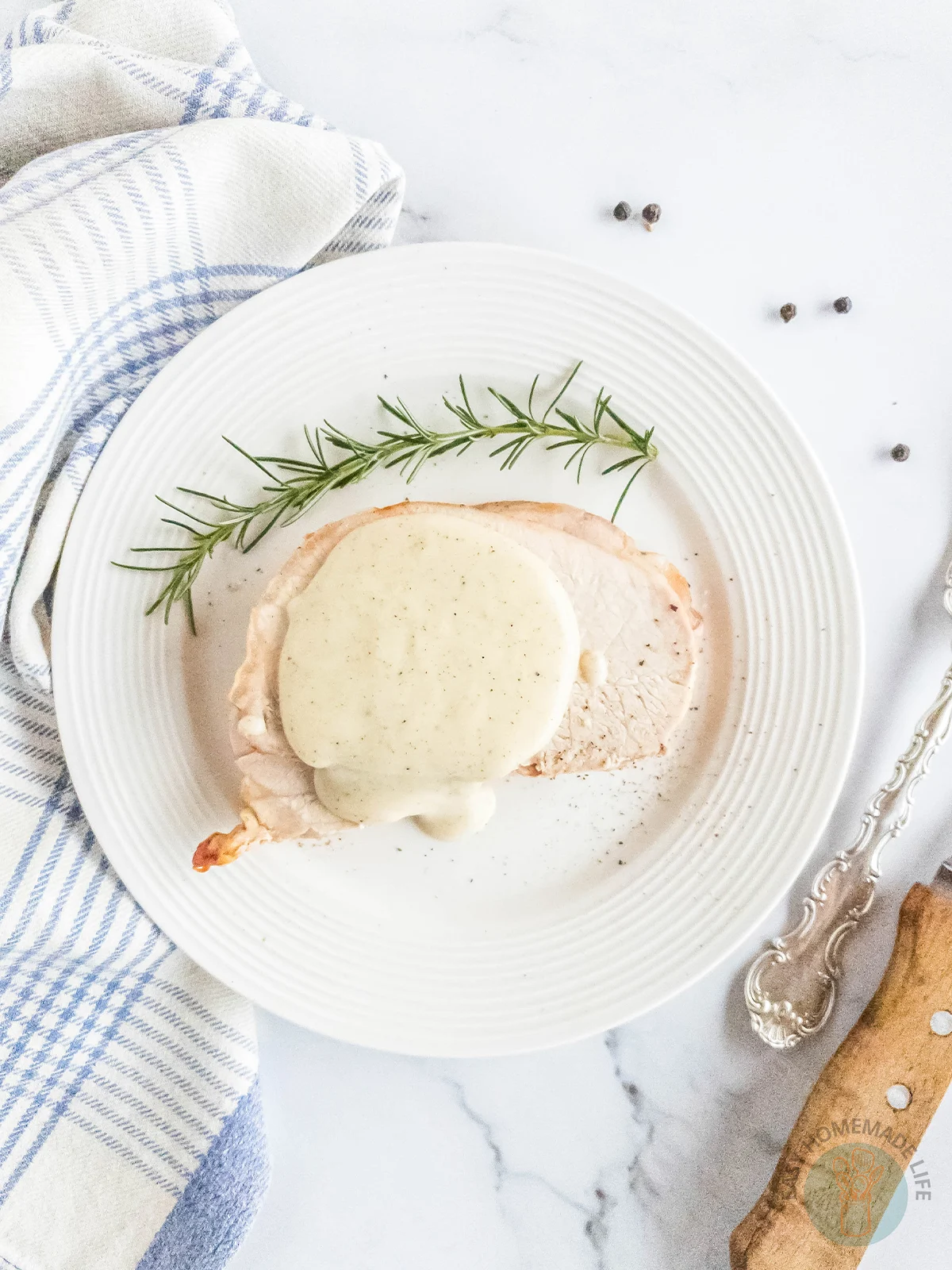 Pepper gravy on slices of meat on a white plate next to a white and blue stripe napkin.