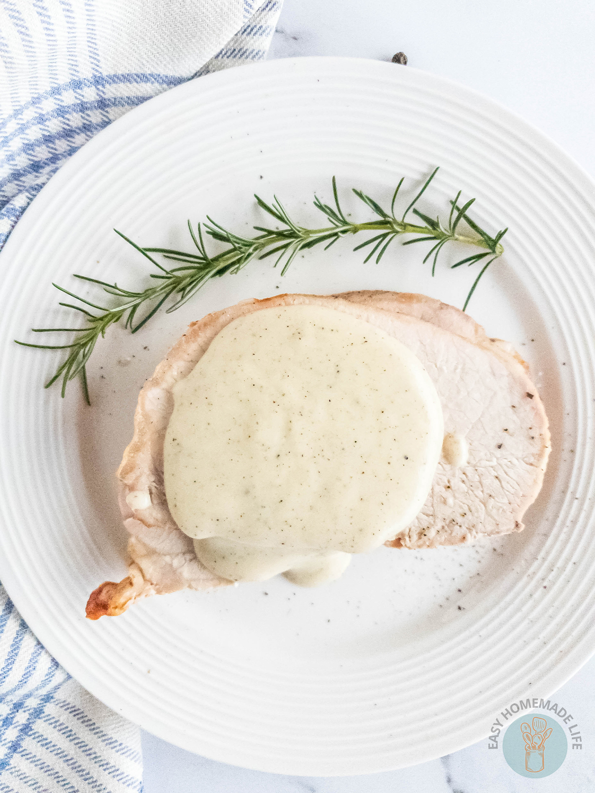 Pepper gravy on slices of meat on a white plate garnished with rosemary.