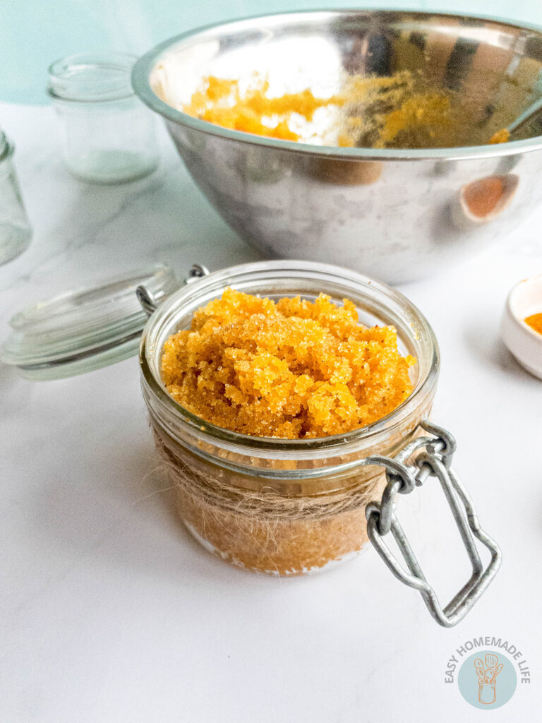 A jar of turmeric body scrub next to a stainless steel bowl.