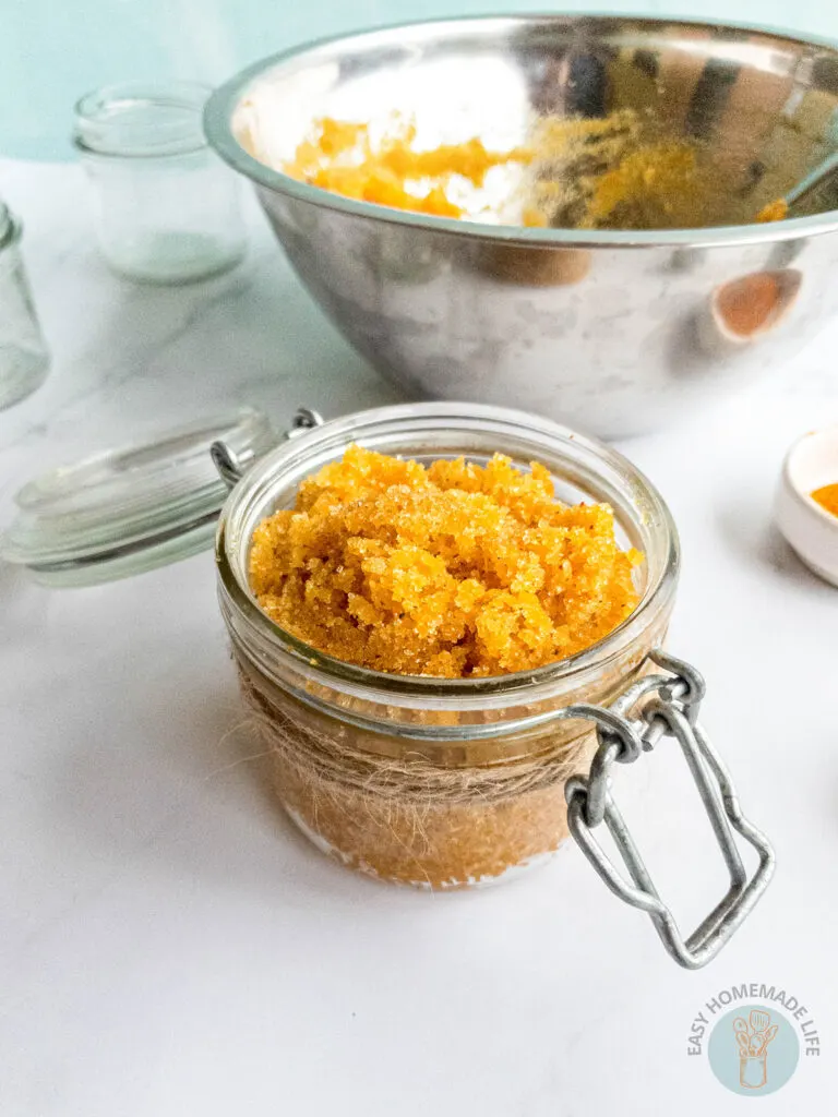 A jar of turmeric body scrub next to a stainless steel bowl.