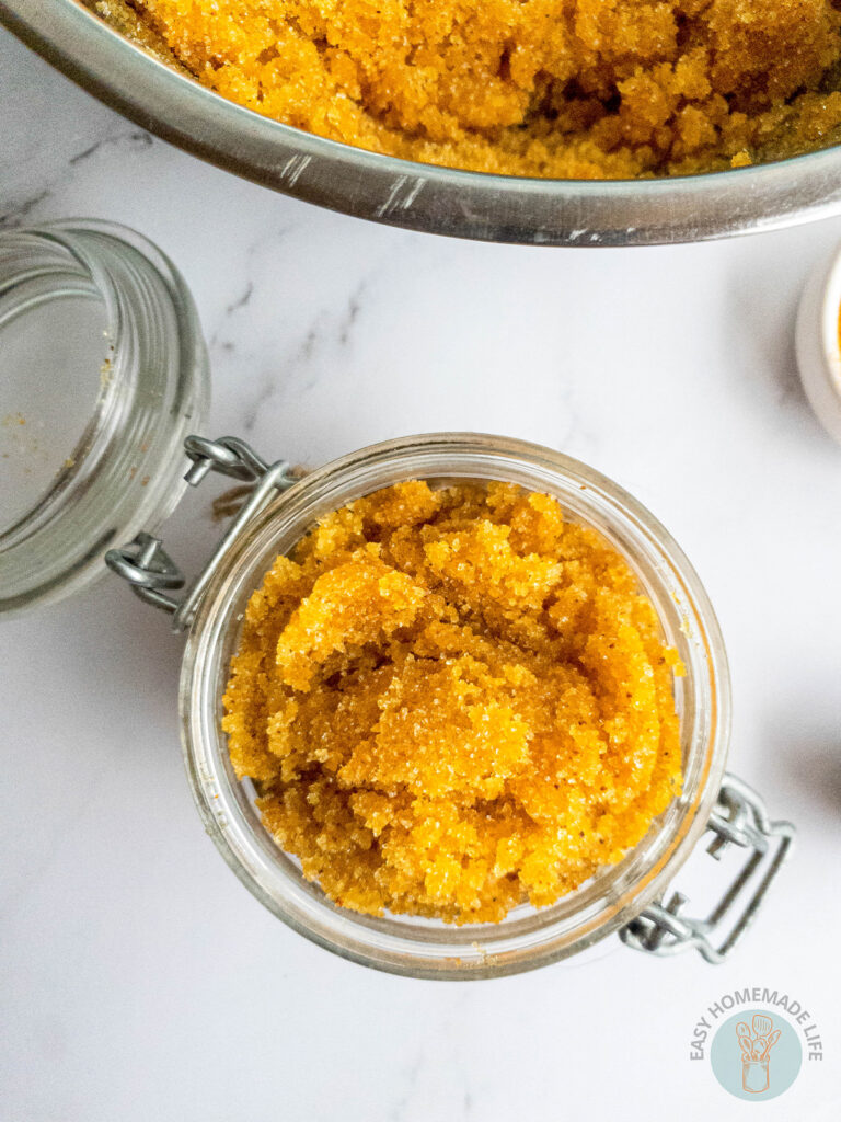 A jar of turmeric body scrub next to a stainless steel bowl containing the same scrub in it.