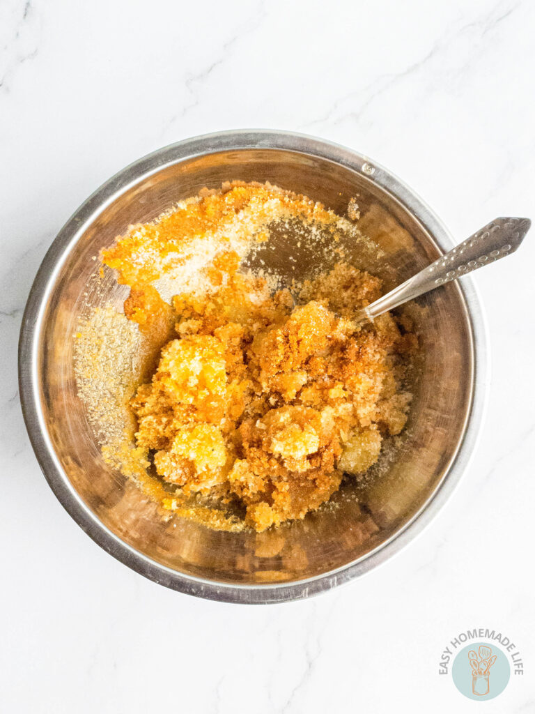 Turmeric body scrub ingredients being mixed in a stainless steel mixing bowl using a spoon.