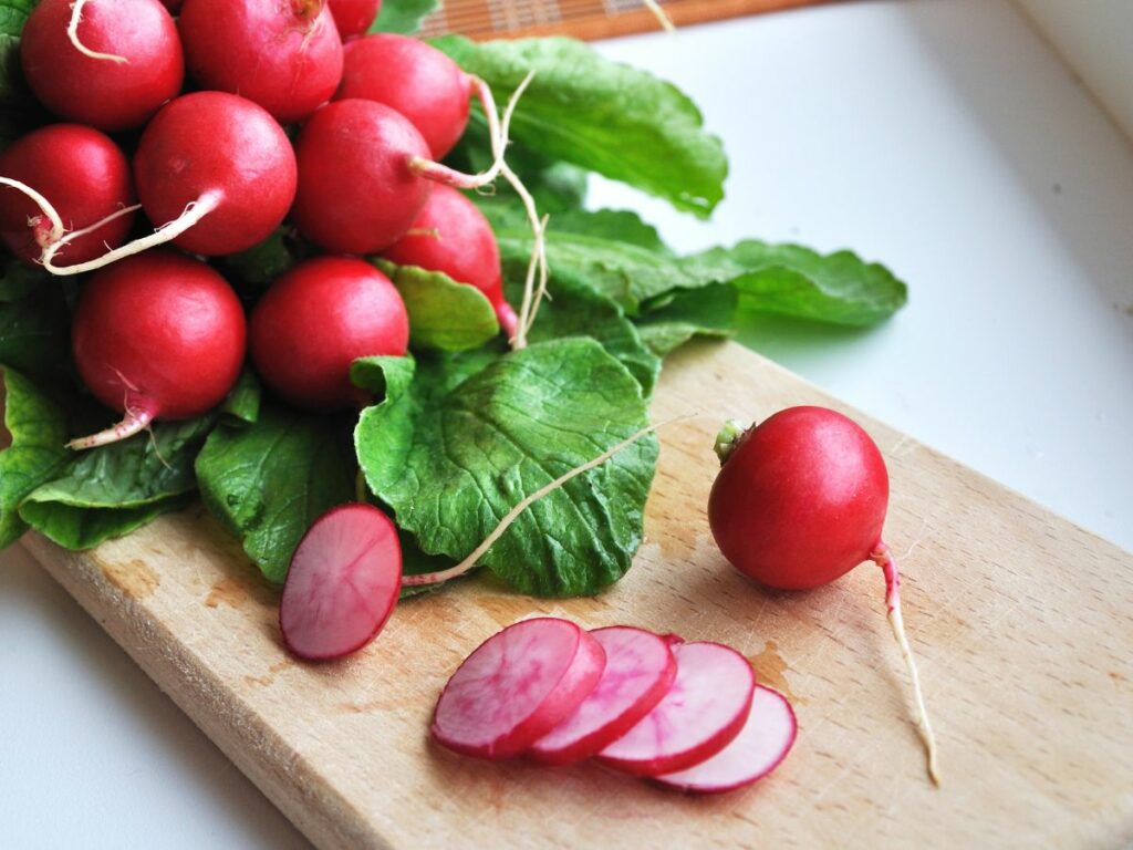 Sliced radishes on a cutting board next to a bunch of fresh unsliced radishes.