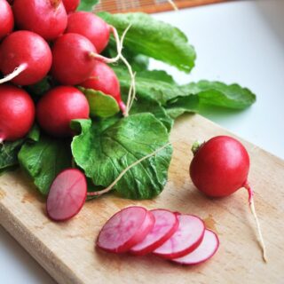 Sliced radishes on a cutting board next to a bunch of fresh unsliced radishes.