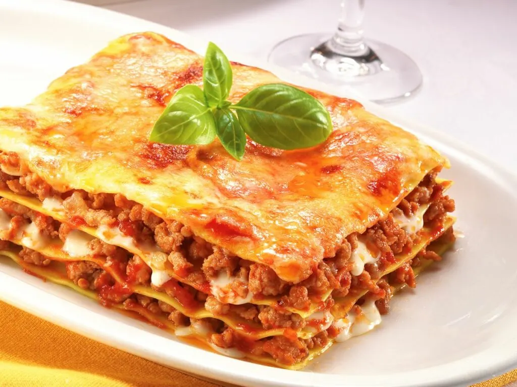 A slice of reheated lasagna on a white plate.