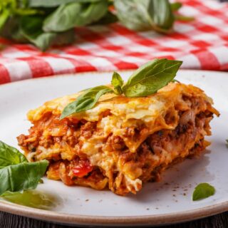 Lasagna portion on a white plate with basil leaves.