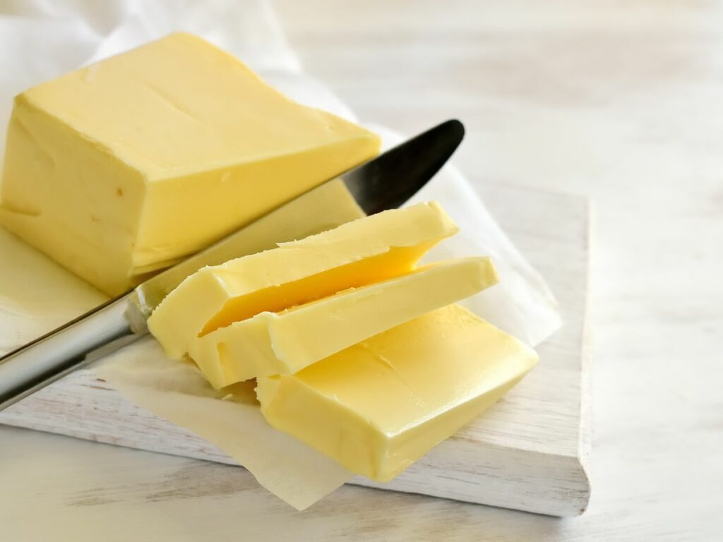 A stick of soft butter with a knife slicing through.