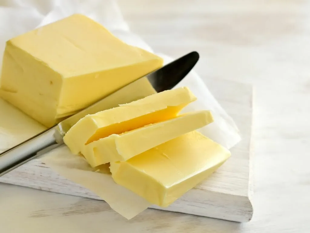 A stick of soft butter with a knife slicing through.