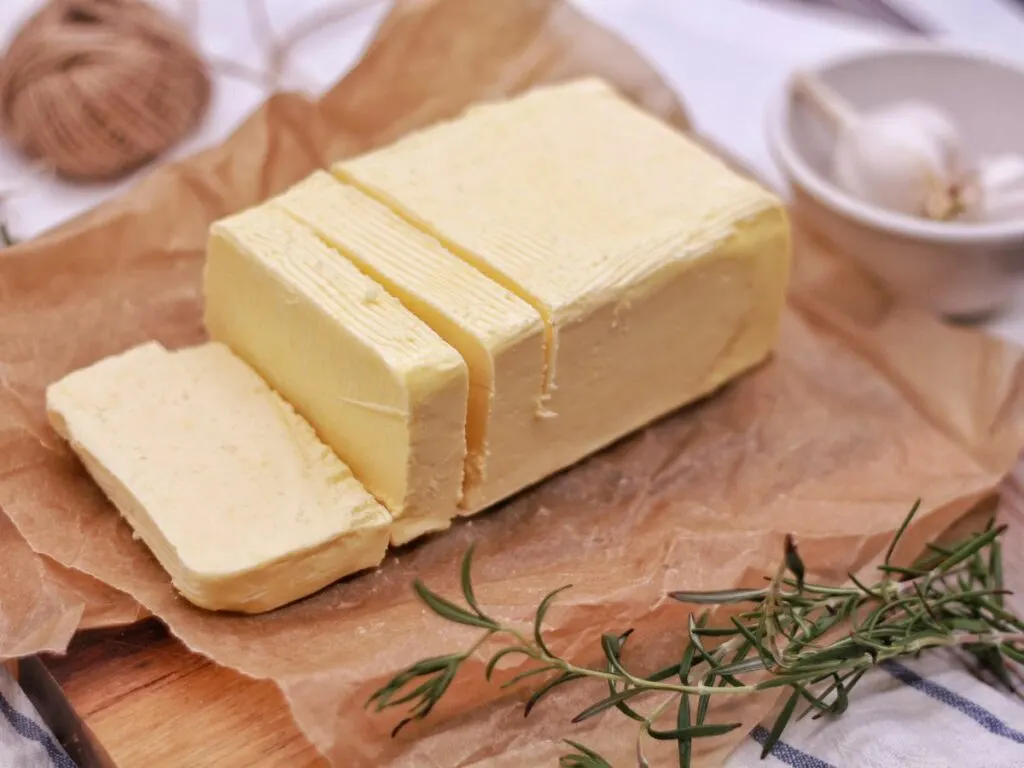 A stick of softened butter cut into slices on a cutting board.