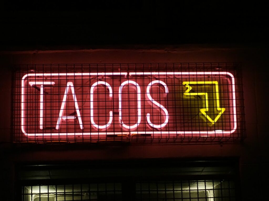 neon sign reading Tacos and a directional down arrow