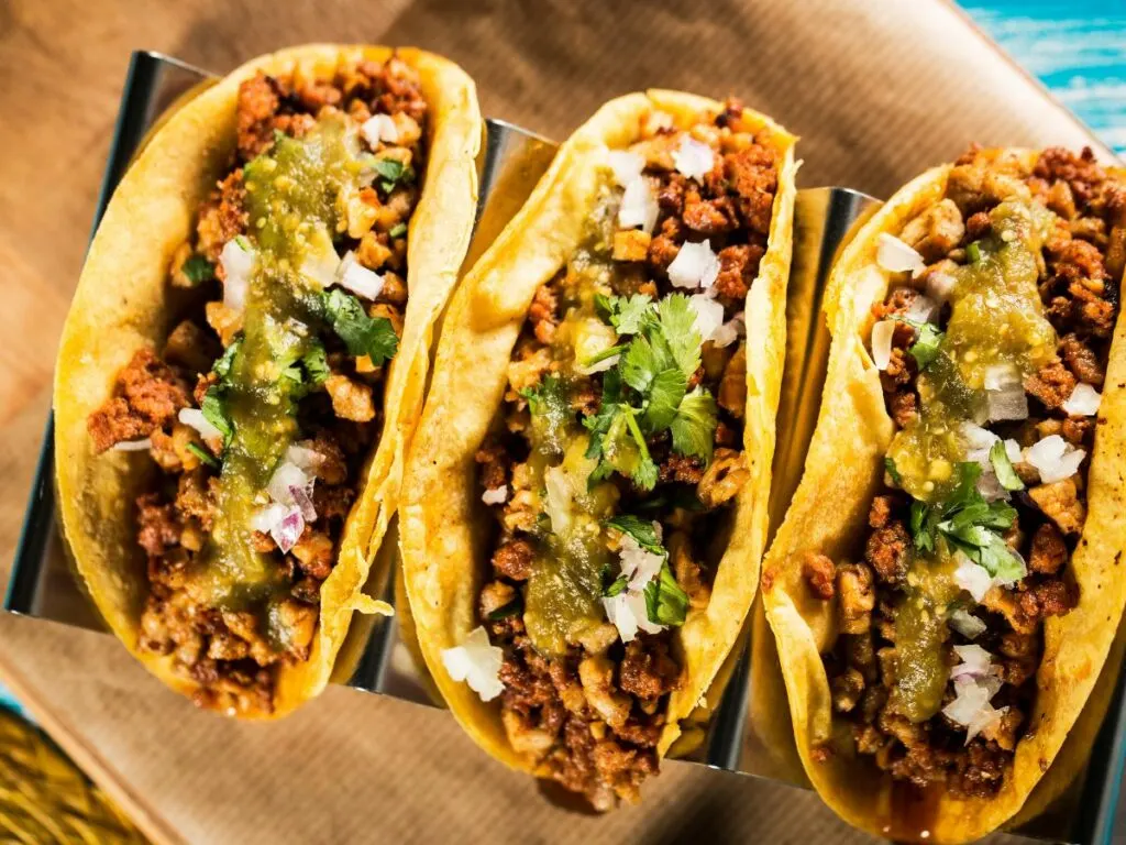 three tacos standing side by side topped with onion cilantro salsa