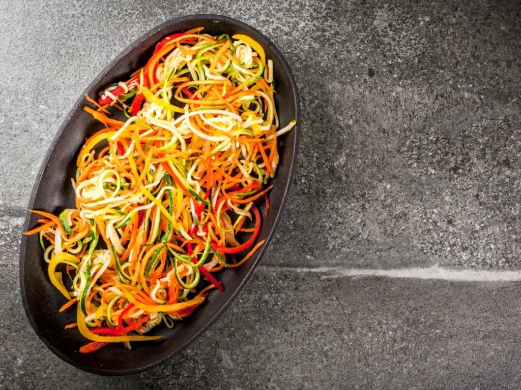 Different color veggie noodles on a black platter.