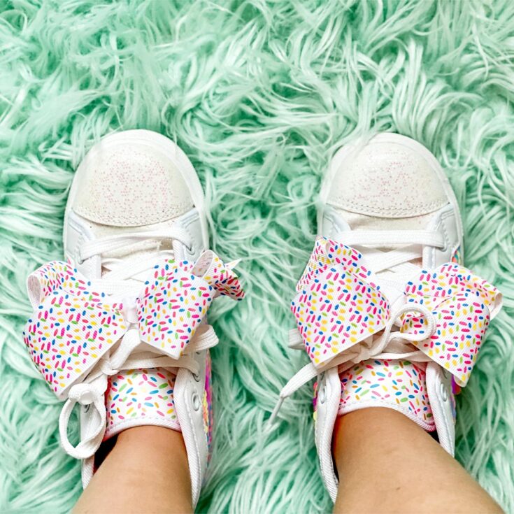 A little girl's white tennis shoes with oversize bow on green shag rug.