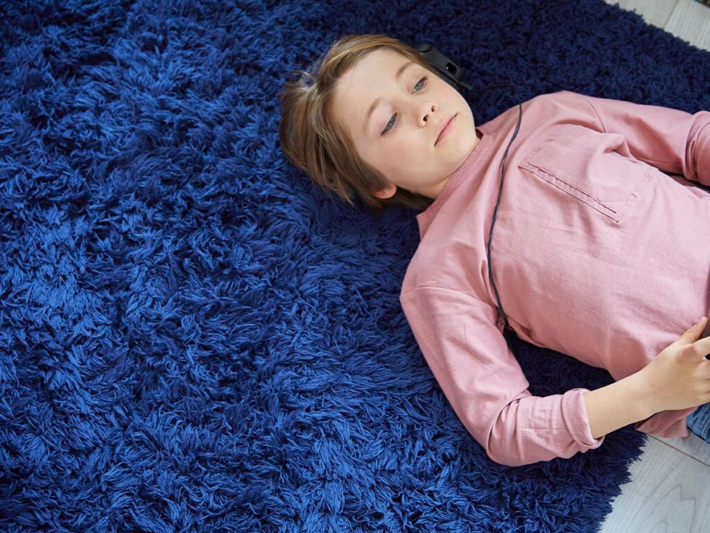 A young boy laying on blue fluffy shag rug.