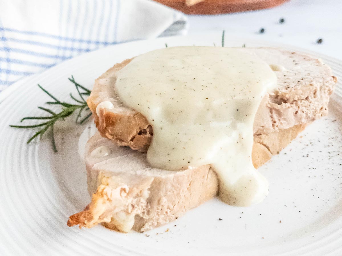 A white plate with two pieces of meat and pepper sauce on it.