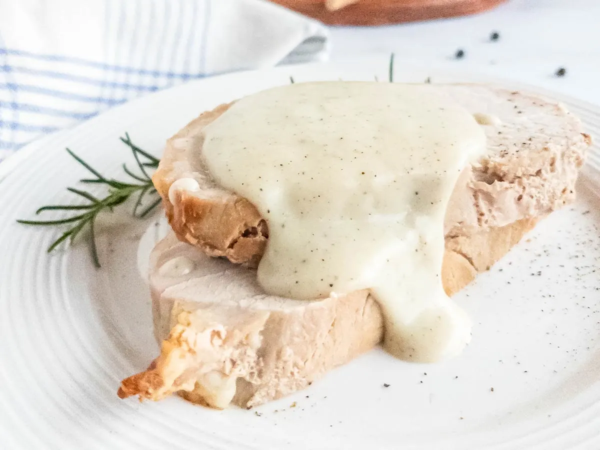 A white plate with two pieces of meat and pepper sauce on it.