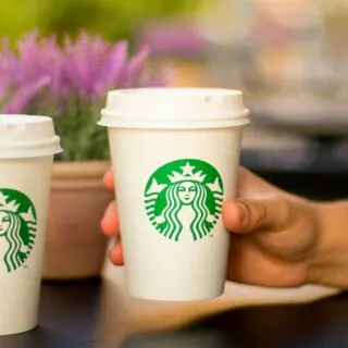 A hand holding a tall cup of starbucks drink.