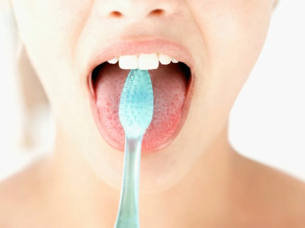 A woman is brushing her tongue to clean it.