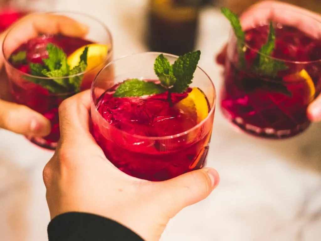Hands of three person each holding a glass of sangria with mint garnish.