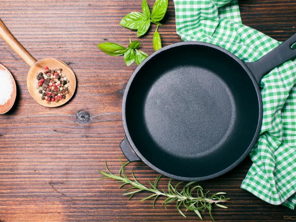 Cast iron skillet with kitchen ingredients and a green hand towel.