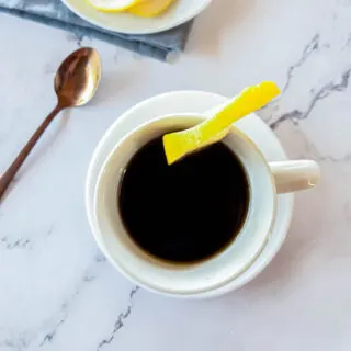 Cafe Romano espresso with lemon garnish and copper stirring spoon.