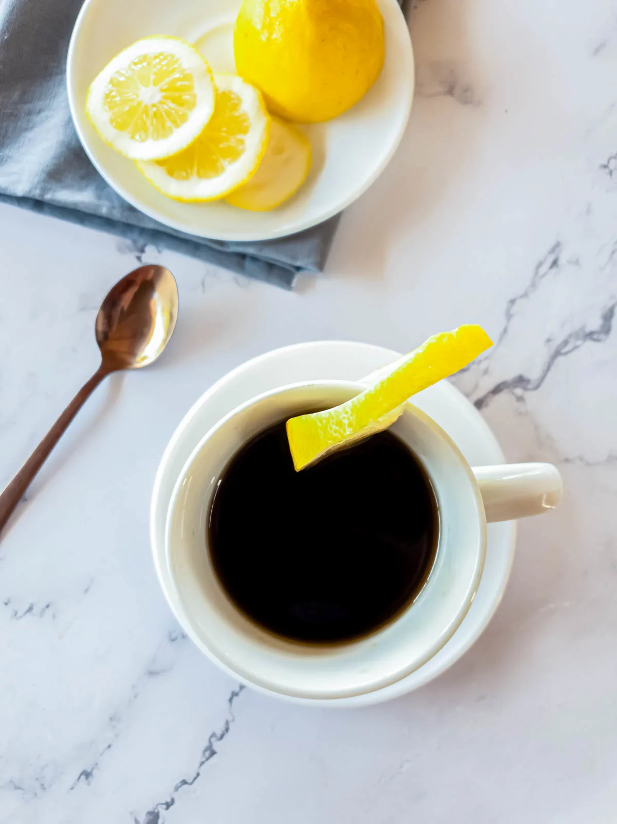 Overhead view of dark espresso with lemon, spoon, plate, and napkin.