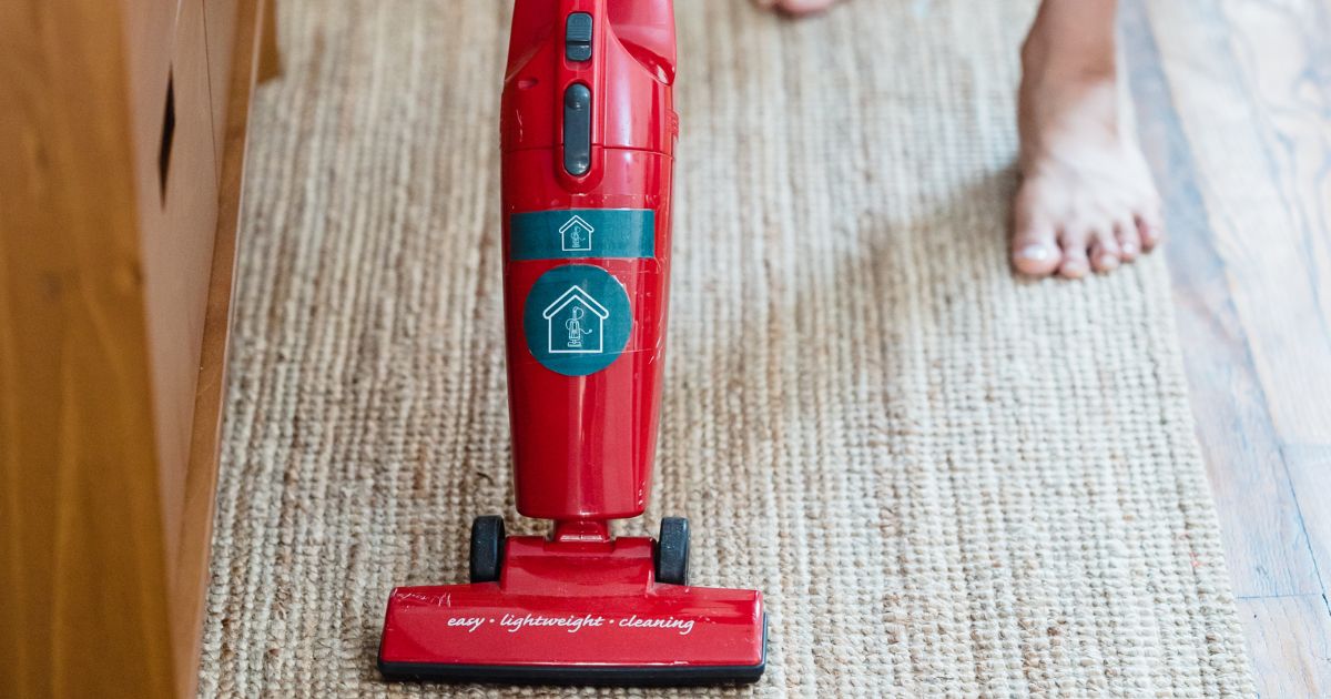 Barefoot woman on tan carpet vacuuming with red vacuum.