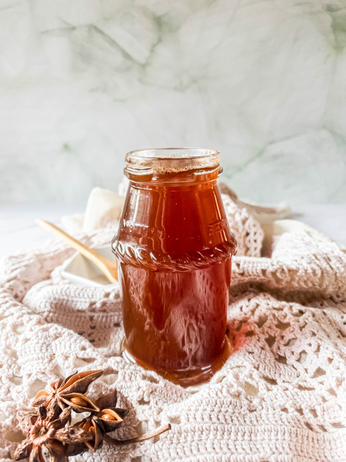 Chai tea simple syrup in recycled glass storage jar with star anise in foreground.